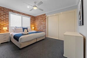 Ein Schlafzimmer mit Bett, Deckenventilator, Kleiderschrank und Backsteinwand.
