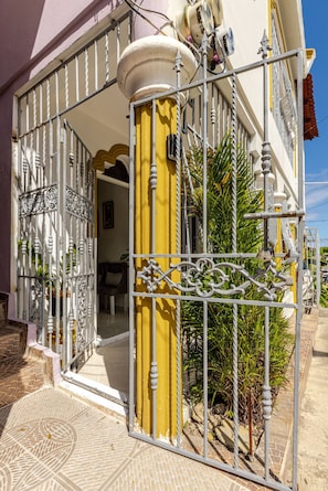 Une entrée fermée par un portail, avec un pilier jaune, un portail en métal et un escalier menant à une porte.