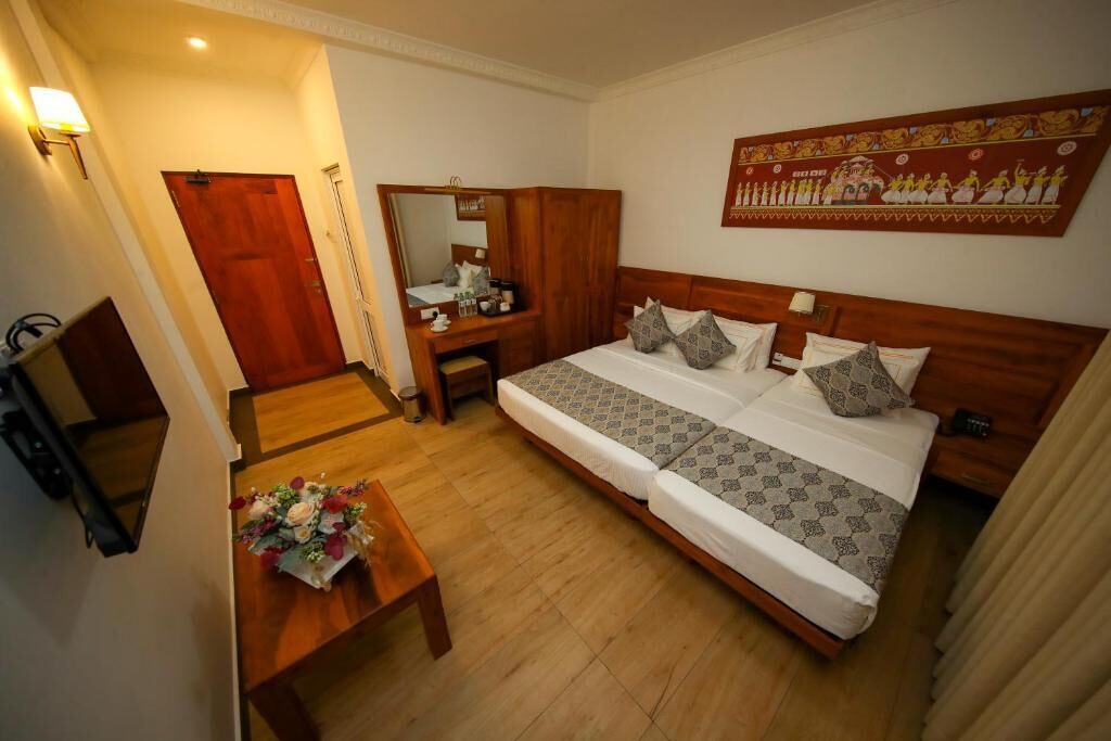 A hotel room with a bed, a desk, a chair, a mirror, a wooden door, and a wall-mounted artwork.