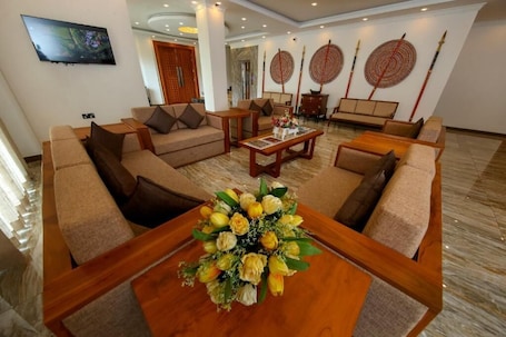 A spacious hotel lobby with sofas, a coffee table with a floral centerpiece, and traditional decor.