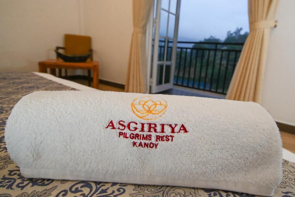 Une serviette blanche roulée, ornée d’une broderie indiquant : « ASGIRIYA PILGRIMS REST KANDY ».