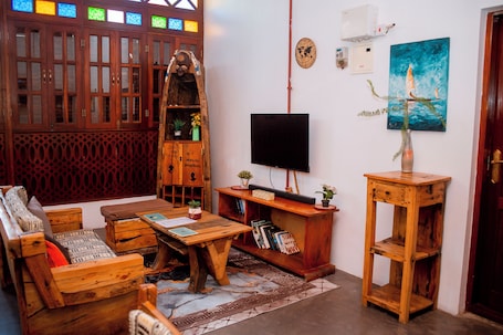 A room with a wooden sofa, a coffee table, a TV, a bookshelf, and a painting.