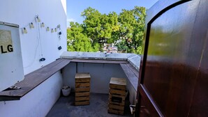 A small balcony with a wooden bench, a white wall with an LG logo, and a view of trees and buildings.