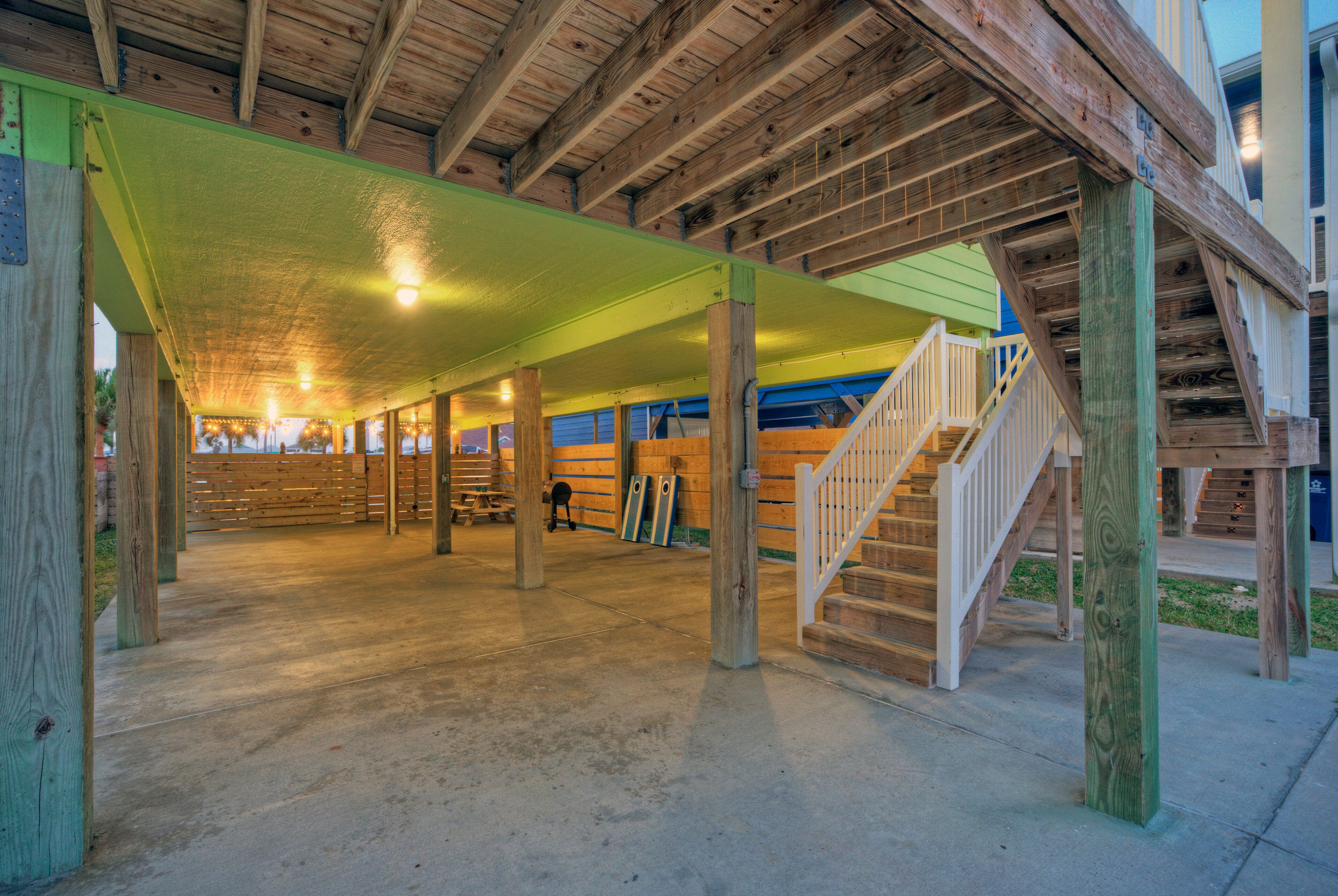 A covered outdoor area with wooden beams, a concrete floor, and a staircase leading to an upper level.