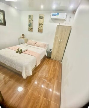 Une chambre à coucher comprenant un lit, une table de chevet, une armoire et un climatiseur fixé au mur.