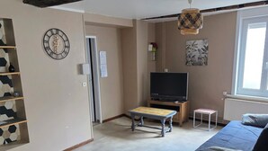 Olohuoneessa on puinen pöytä, sohva, televisio ja koristeellinen seinäkello.