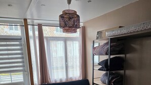 Huoneessa on sohva, kerrossänky, riippuvalaisin ja ikkuna, jossa on verhot.