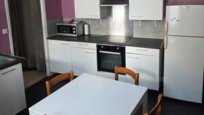 Kompakti keittiö, jossa on valkoiset kaapit, sisäänrakennettu uuni, mikroaaltouuni ja jääkaappi.