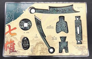 En samling traditionelle kinesiske artefakter, herunder et sværd, et skjold og andre ceremonielle genstande, præsenteret foran et baggrund med kinesisk kalligrafi.