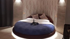 Un letto rotondo con una coperta blu, un comodino con una bottiglia e due luci a parete.