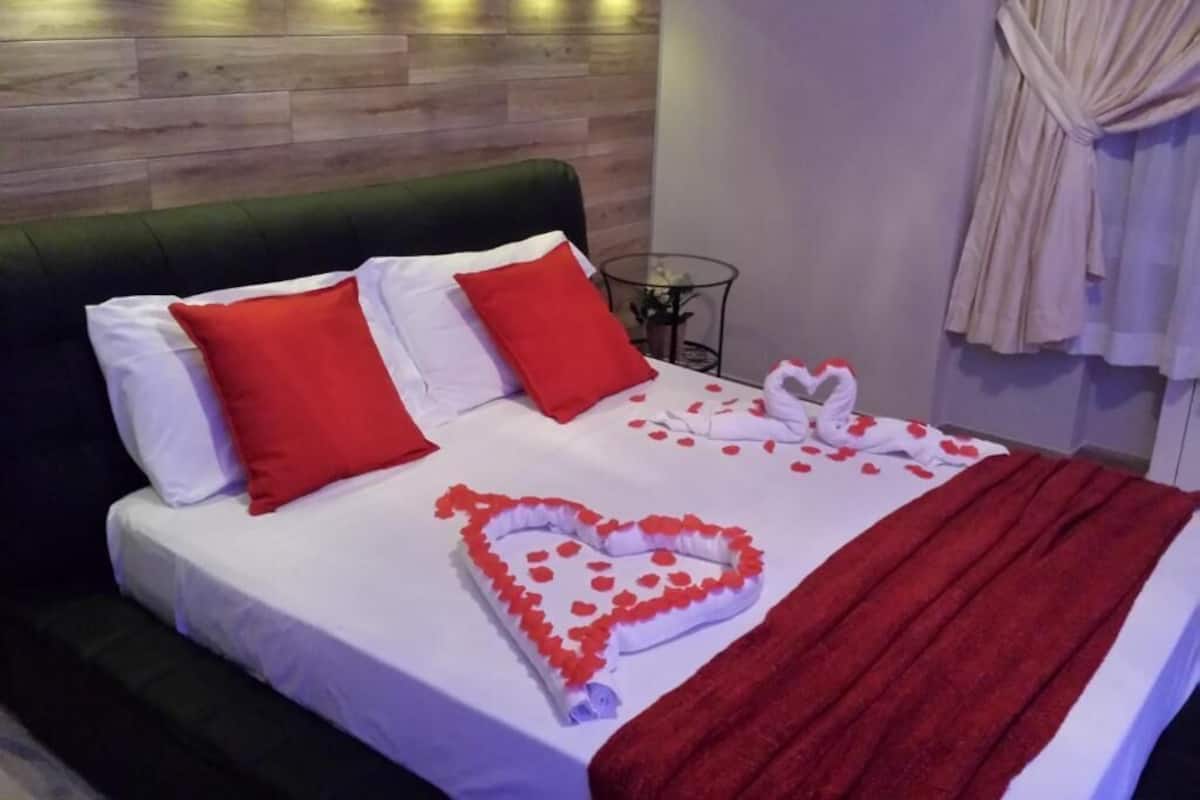 A bed with white bedding, red pillows, and a heart-shaped decoration made of rose petals.