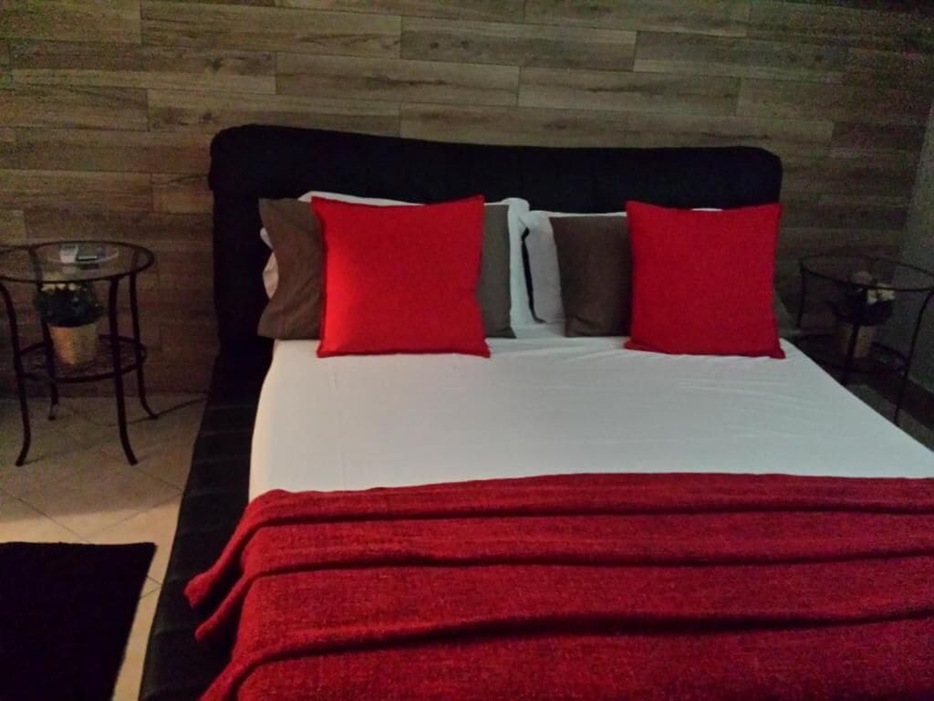 Ein Bett mit roter und weißer Bettwäsche, ein dunkles Kopfteil und eine Holzwand dahinter.