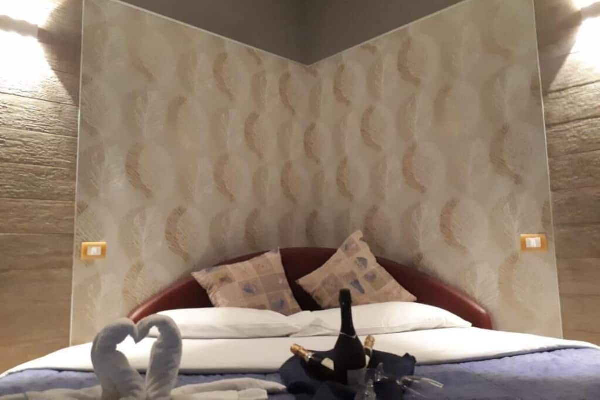 A hotel room with a patterned wallpaper, a bed with red headboard, and a heart-shaped decoration on the bed.