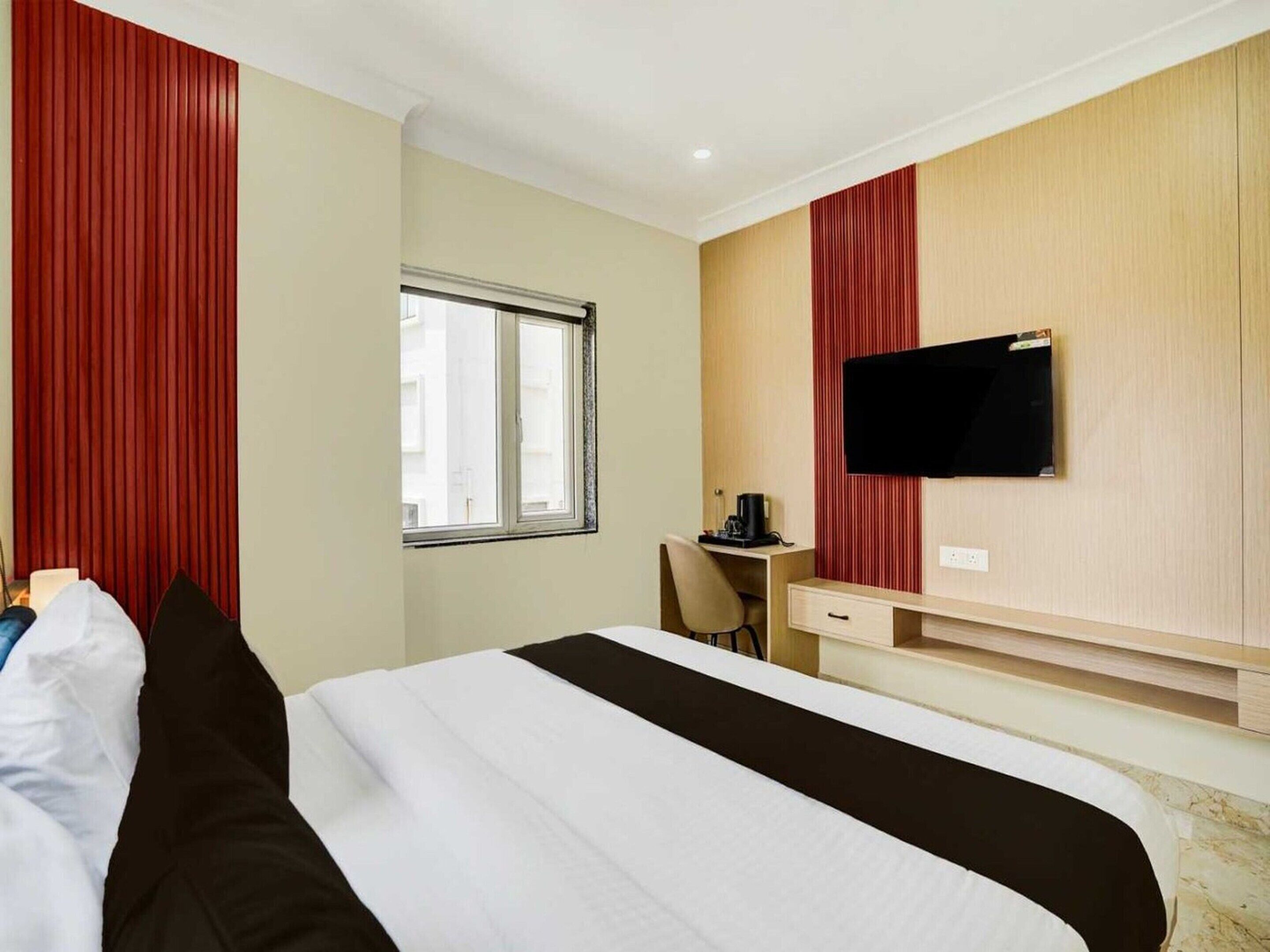 Habitación de hotel con cama, escritorio, silla, televisión y ventana.