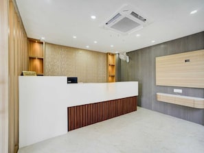 Un comptoir d’accueil avec une pancarte indiquant les heures d’arrivée et de départ, un ventilateur fixé au mur et une bouche d’aération au plafond.