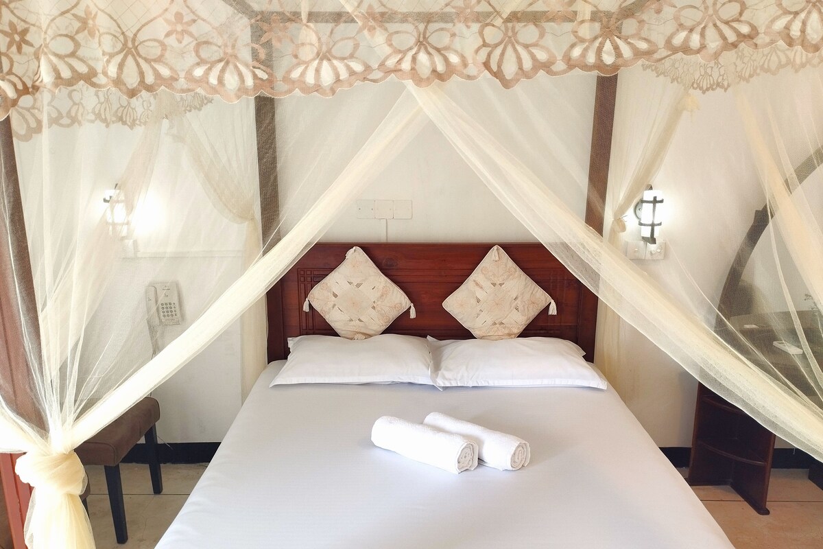 A bed with a canopy, pillows, and a rolled towel.