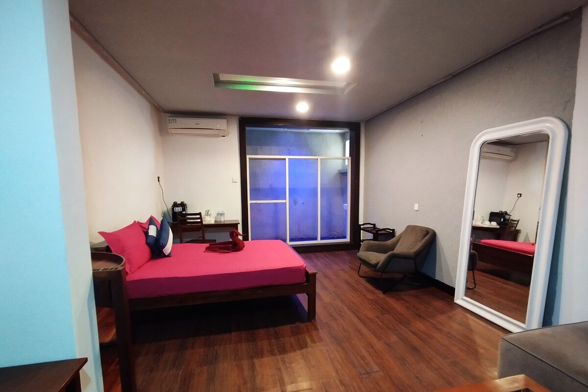 A bedroom with a bed, a chair, a desk, a window, and an air conditioning unit.