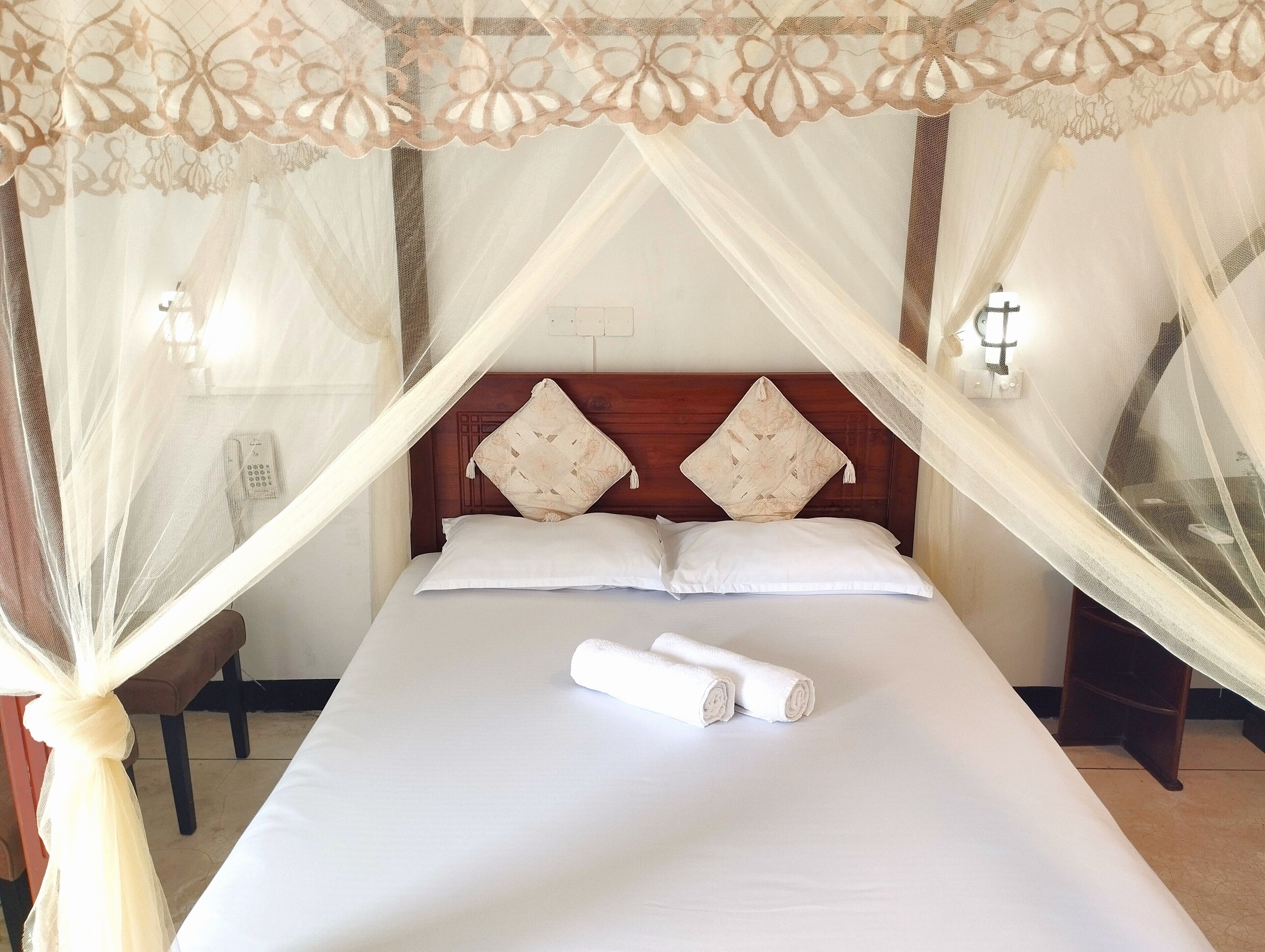 A bed with a canopy, pillows, and a rolled towel.