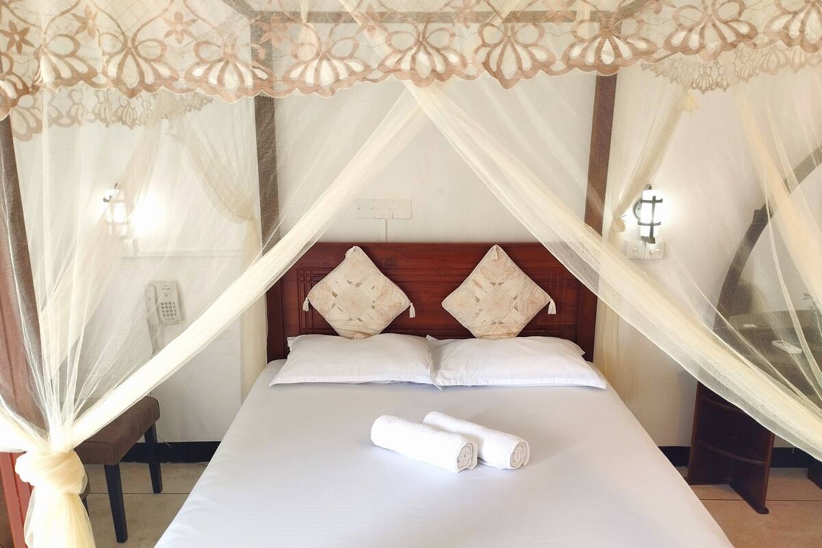 A bed with a canopy, pillows, and a rolled towel.