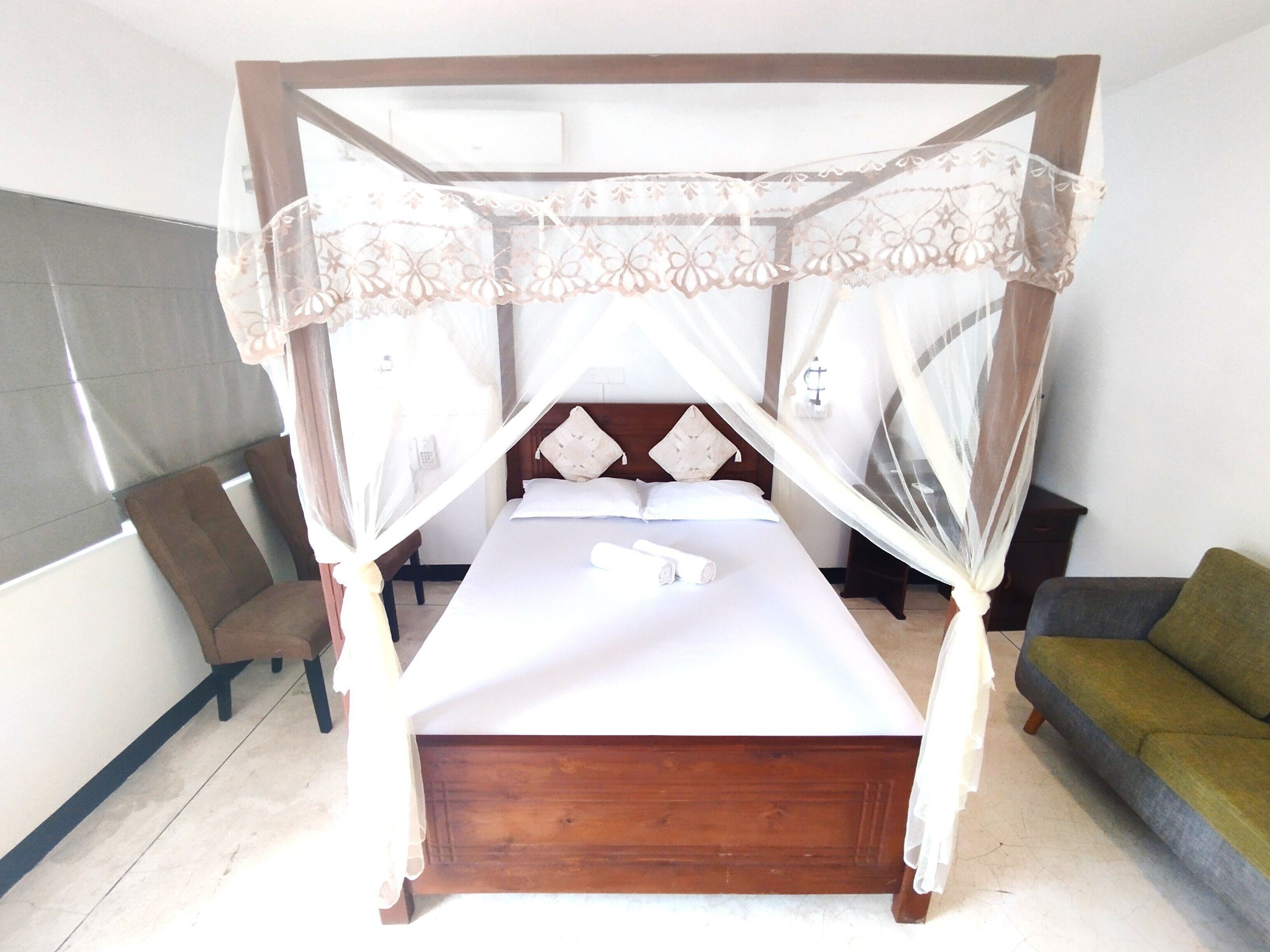 Una stanza con letto a baldacchino, una sedia, un divano e una finestra con tende.