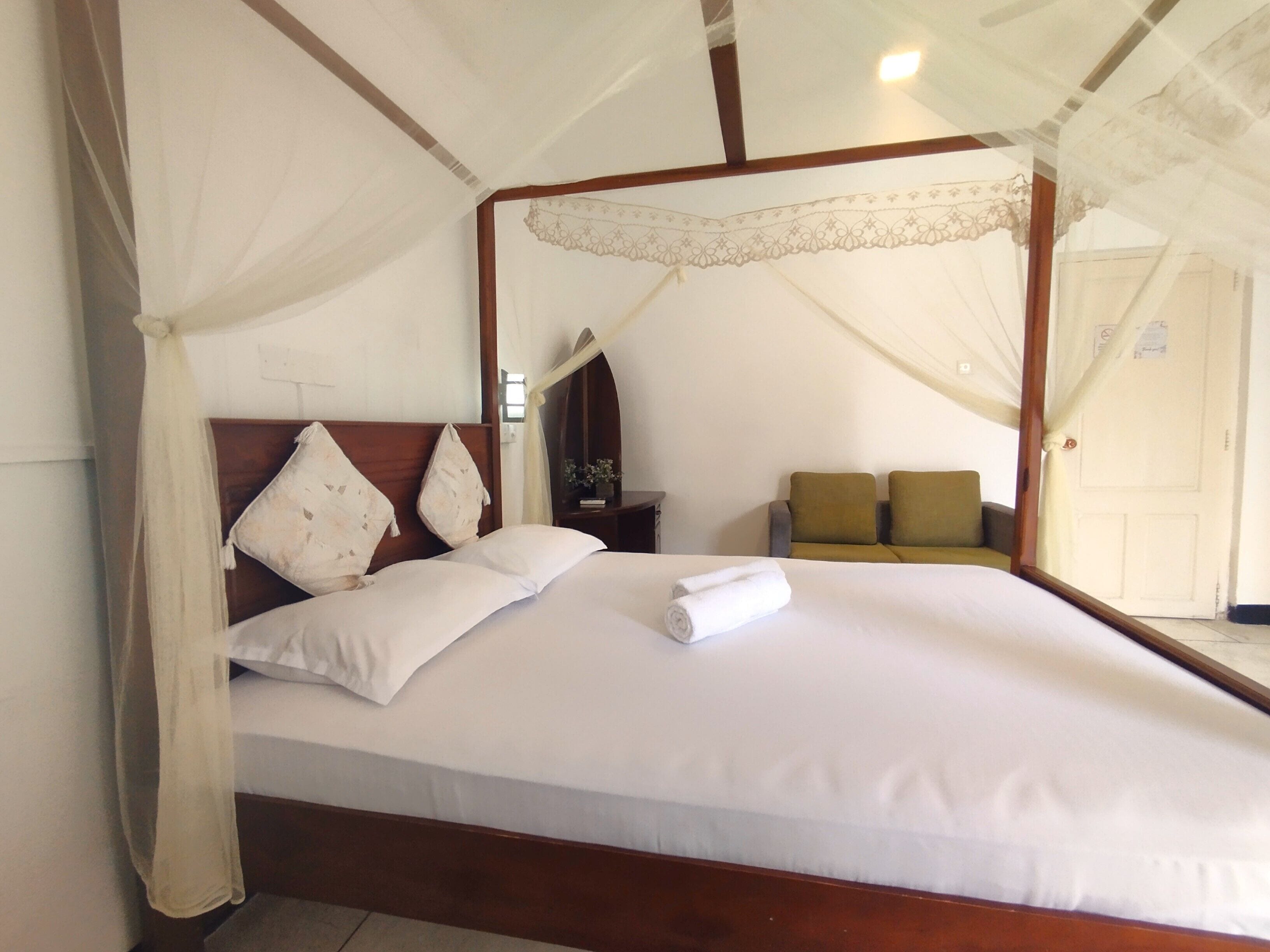 A bed with a canopy, pillows, a bedside table, and a sofa in a hotel room.