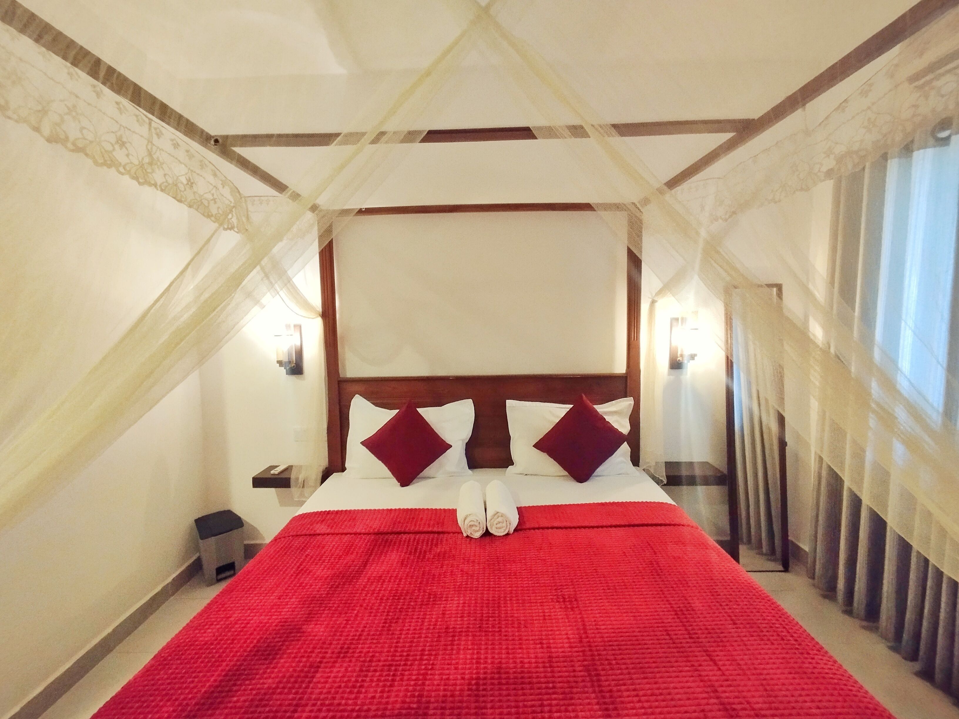 A hotel room with a four-poster bed, a red bedspread, and a canopy.