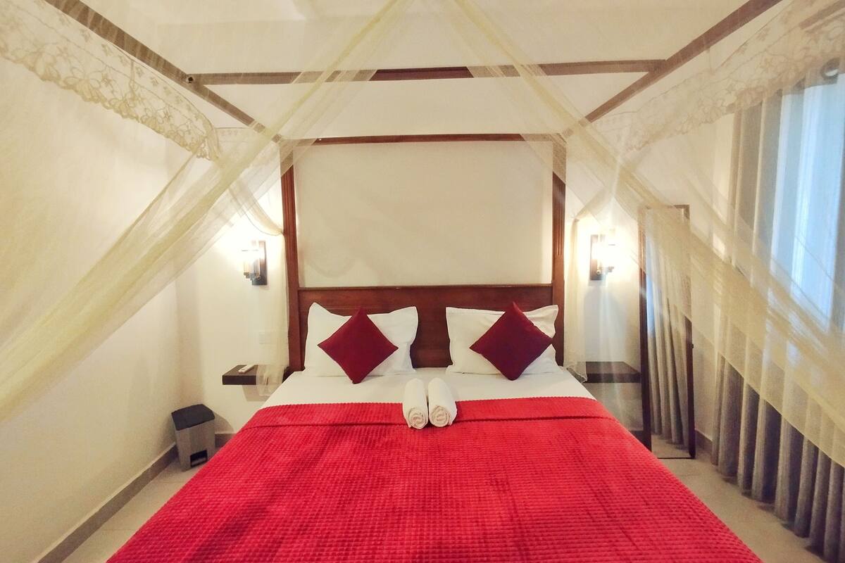 A hotel room with a four-poster bed, a red bedspread, and a canopy.