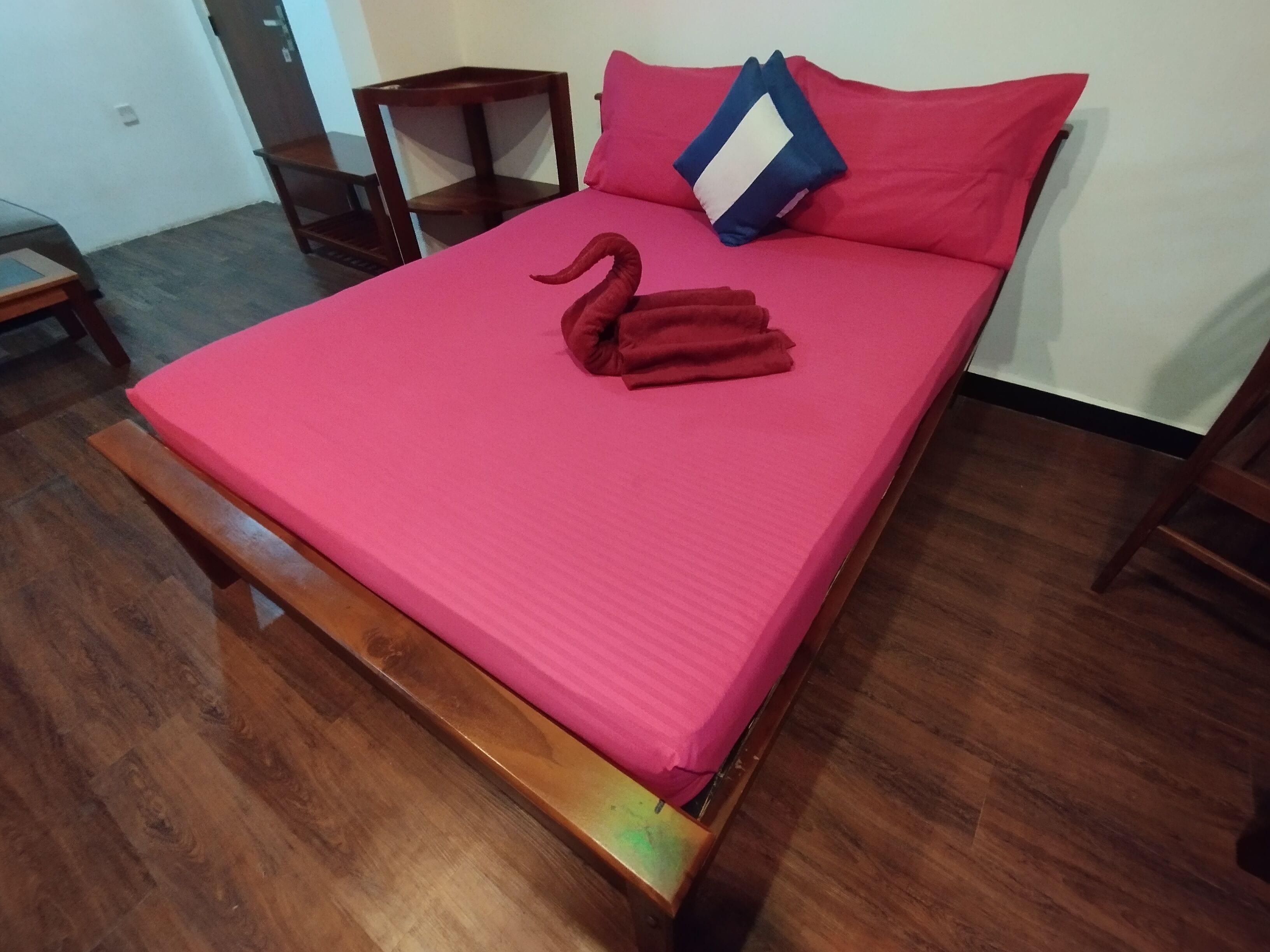 A bed with a pink mattress, a wooden headboard, and a red swan-shaped pillow.