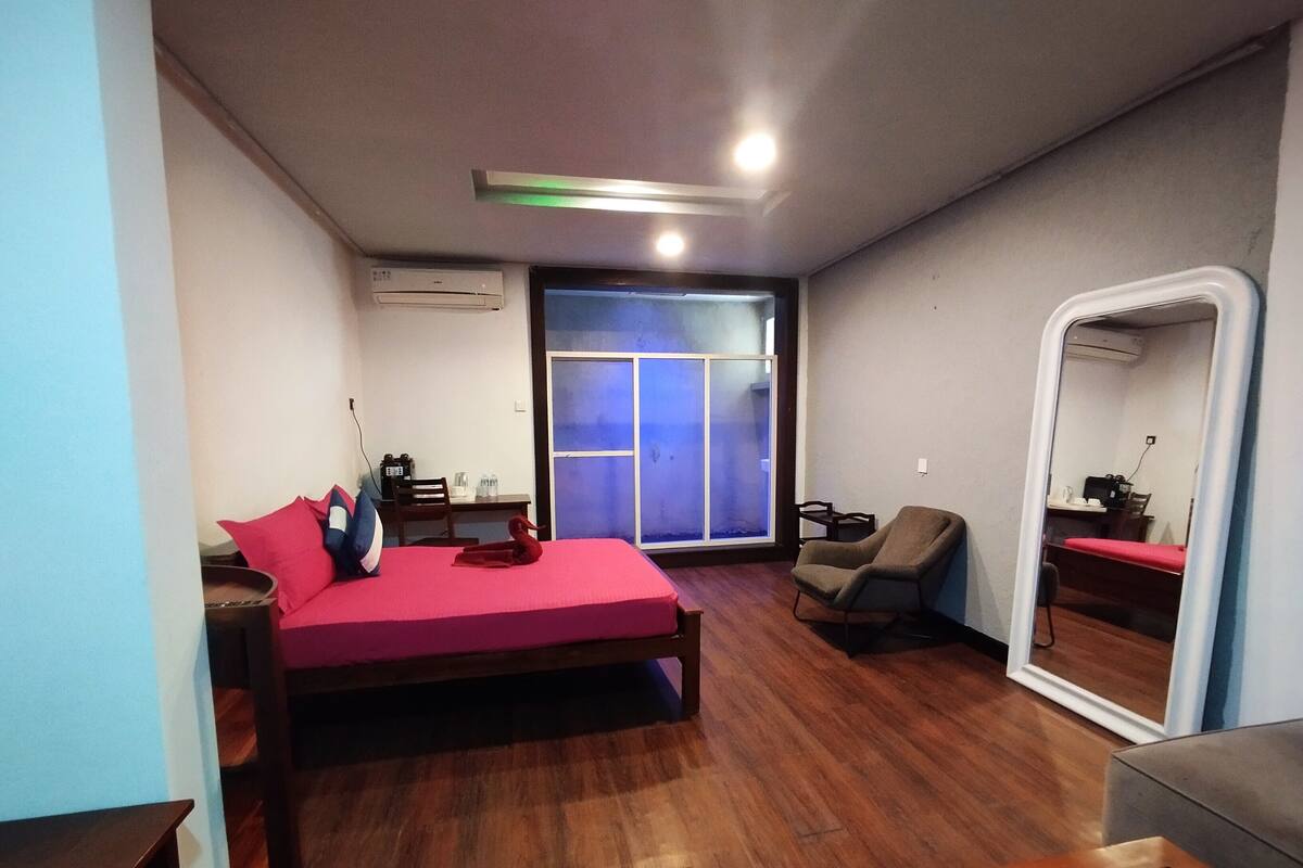 A bedroom with a bed, a chair, a desk, a window, and an air conditioning unit.