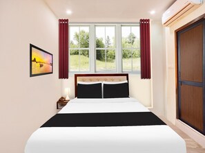 Quarto com cama, mesa de cabeceira, luminária, janela com cortinas e um quadro na parede.