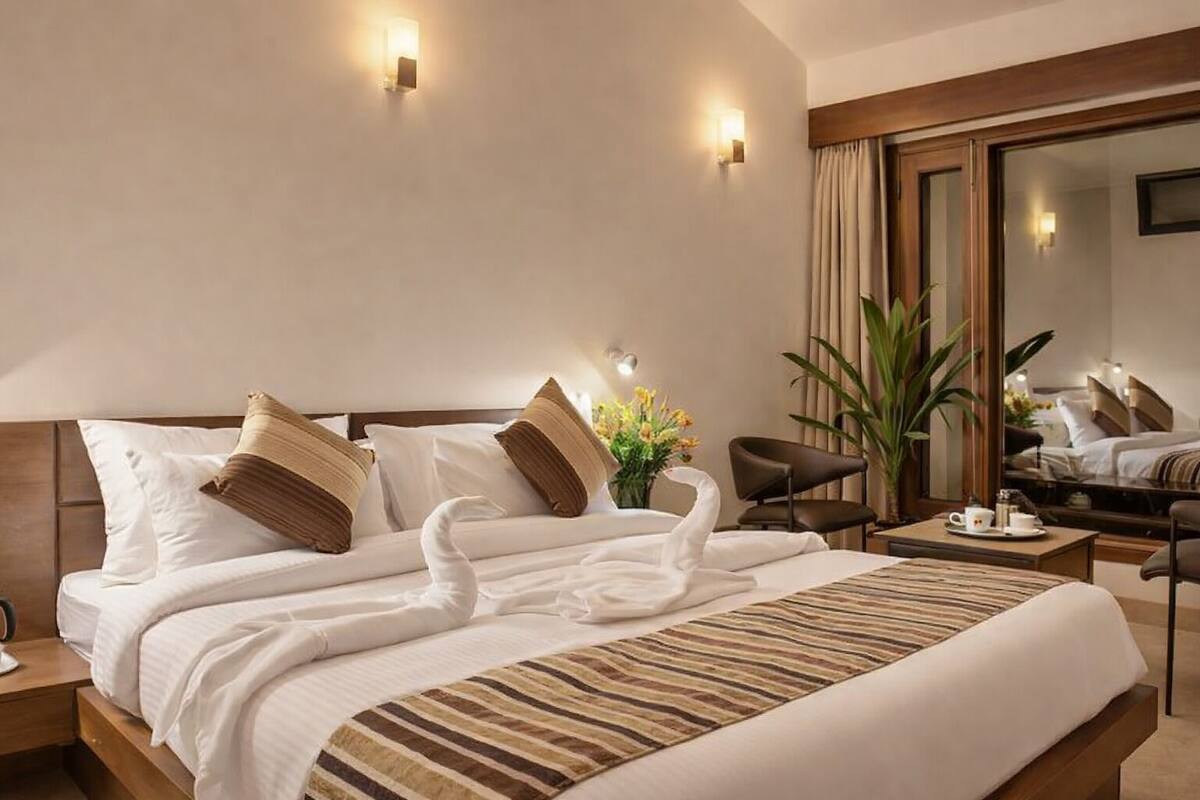 Habitación de hotel con una cama grande, dos apliques de pared, un espejo, un escritorio y una silla.