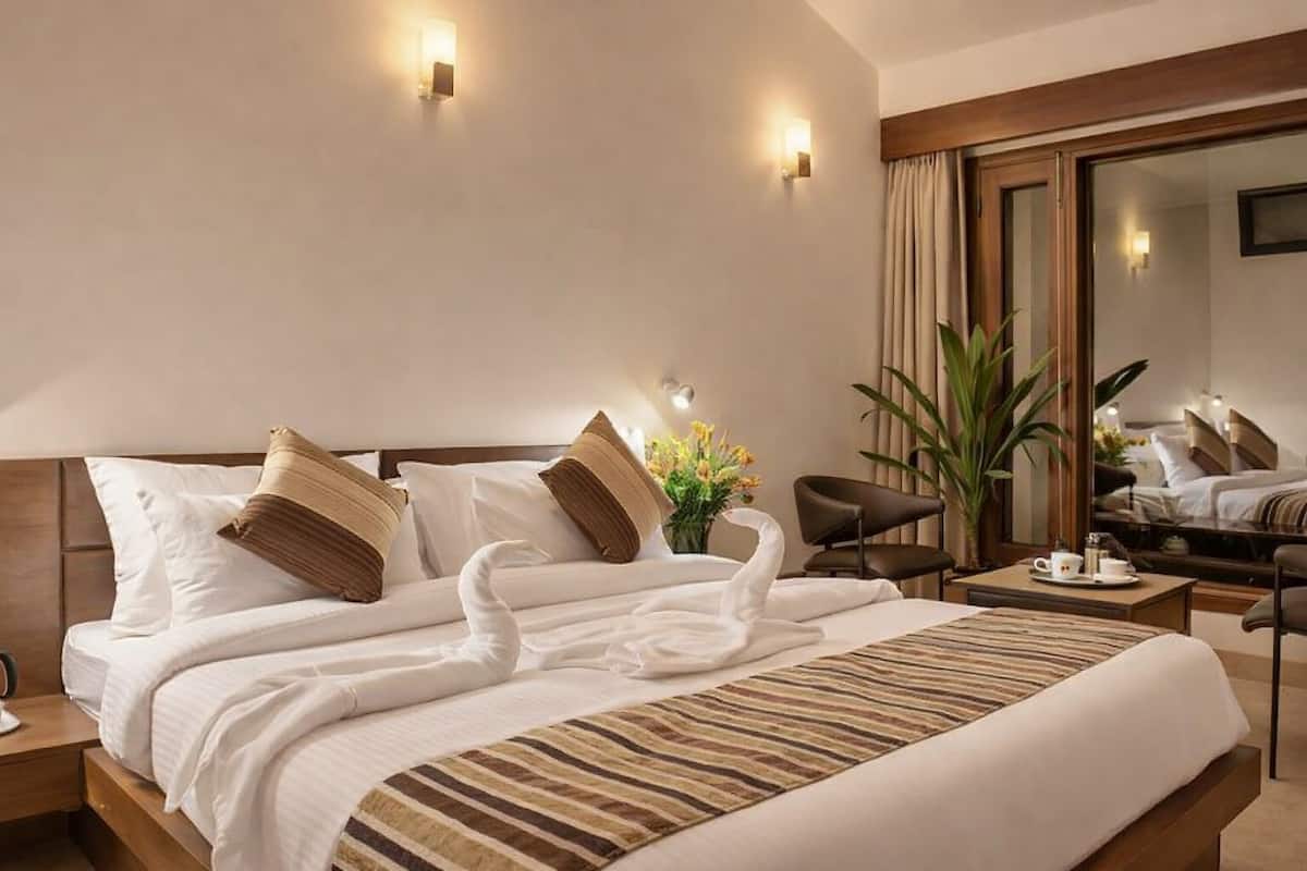 Ett hotellrum med en stor säng, två vägglampor, en spegel, ett skrivbord och en stol.