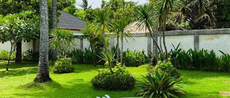 A well-maintained garden with a white surfboard, palm trees, and a building with a tiled roof.