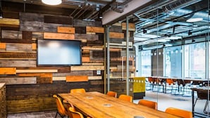 A conference room with a long wooden table, orange chairs, a large screen, and a rustic wall design. - Student Only Studio Chapter Lewisham (London)