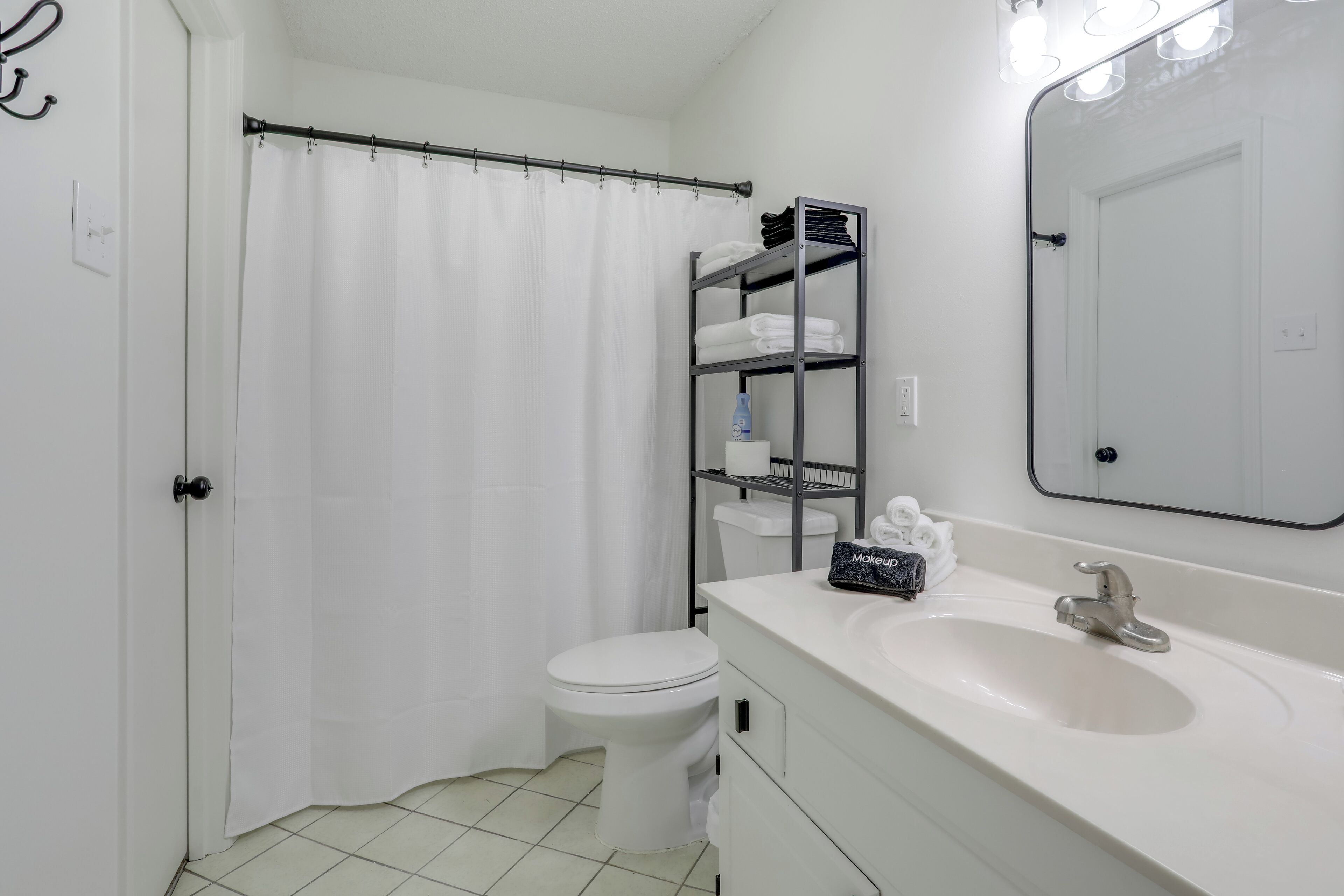Een badkamer met toilet, wastafel, spiegel, douchegordijn en een plank met handdoeken.