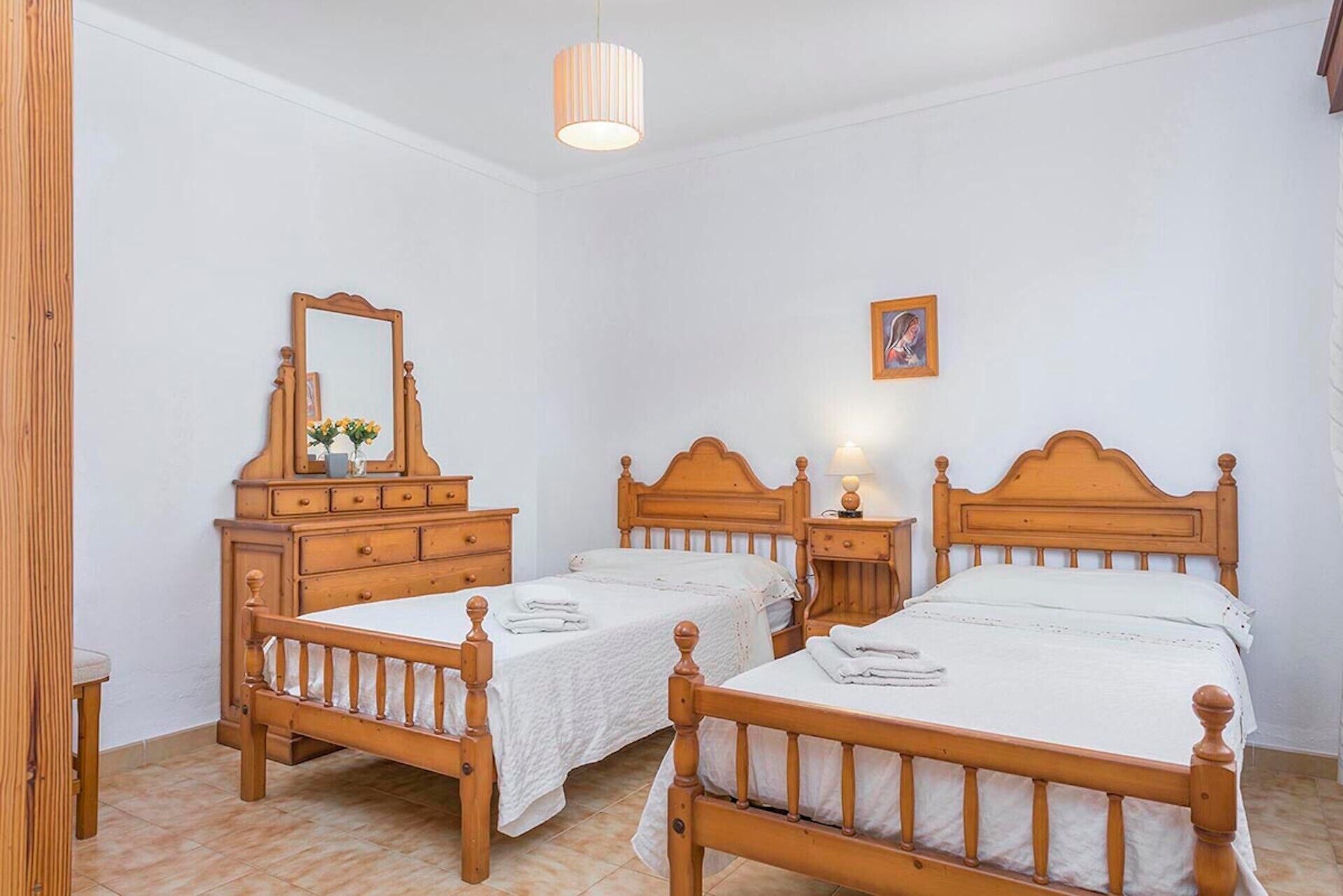 A bedroom with two wooden beds, a dresser, a mirror, and a hanging light fixture.