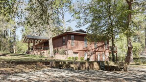 A log cabin with a porch and a small deck, surrounded by trees and a gravel path. - Near Bruce's Field, Downtown & Hospital! Cozy Unit (Aiken)