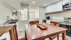 A modern kitchen with white cabinets, stainless steel appliances, a wooden dining table, and a built-in oven. - Near Bruce's Field, Downtown & Hospital! Cozy Unit (Aiken)