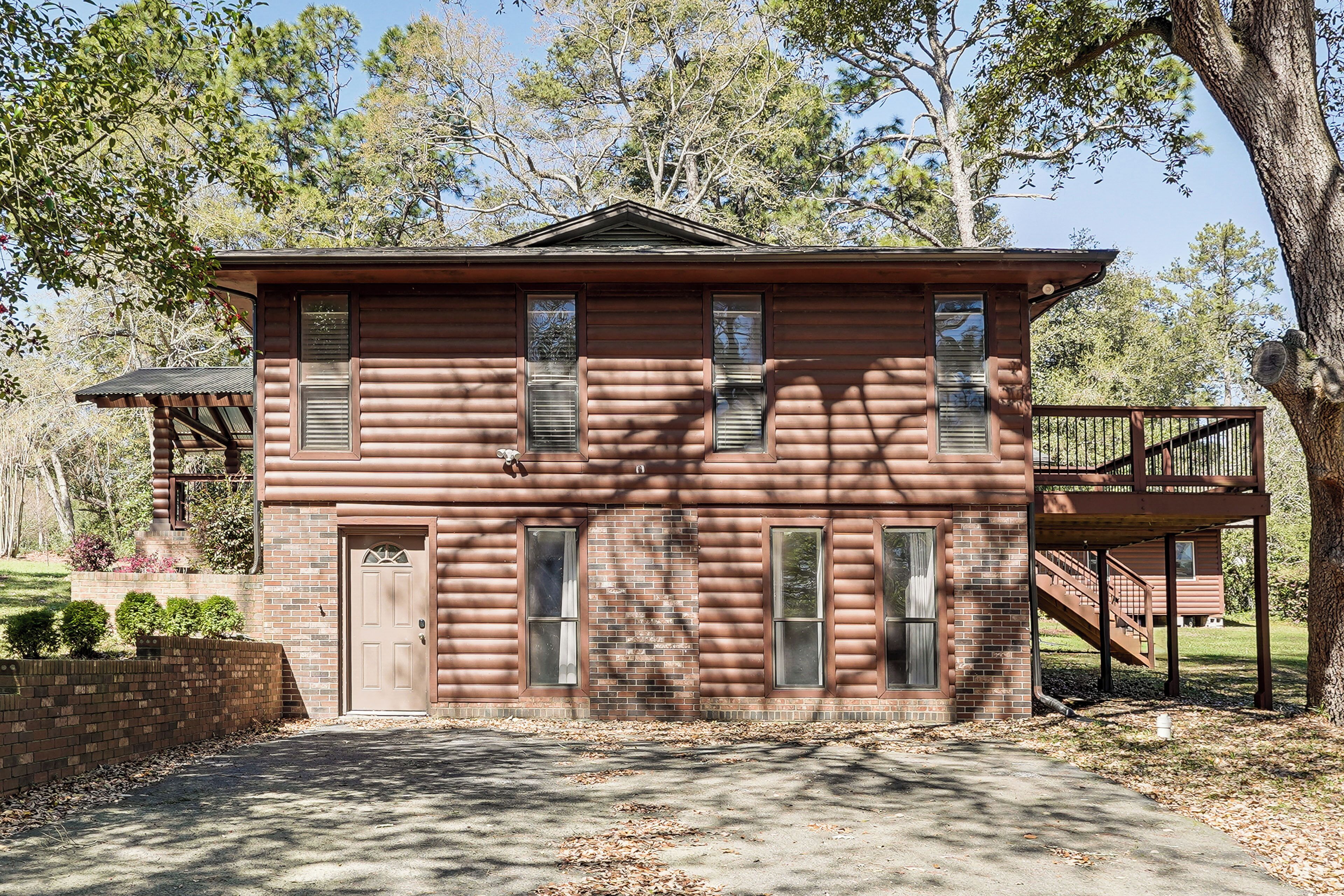 A two-story log cabin with a front porch, a staircase to an upper level, and a brick foundation.