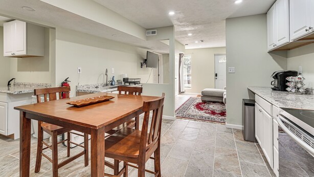 A modern kitchen with a dining area, white cabinets, granite countertops, and a tiled floor. - Near Bruce's Field, Downtown & Hospital! Cozy Unit (Aiken)