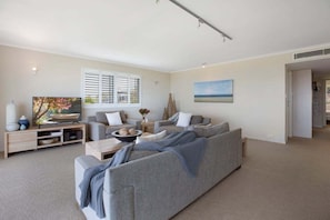 A modern living room with a grey sofa, a flat-screen TV, and a painting on the wall. - Captivating ocean views - Eagles Retreat  (Noosa)