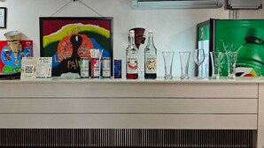 Un coin bar agrémenté d’un tableau coloré, de bouteilles d’alcool, de verres et d’une bouteille de soda verte.