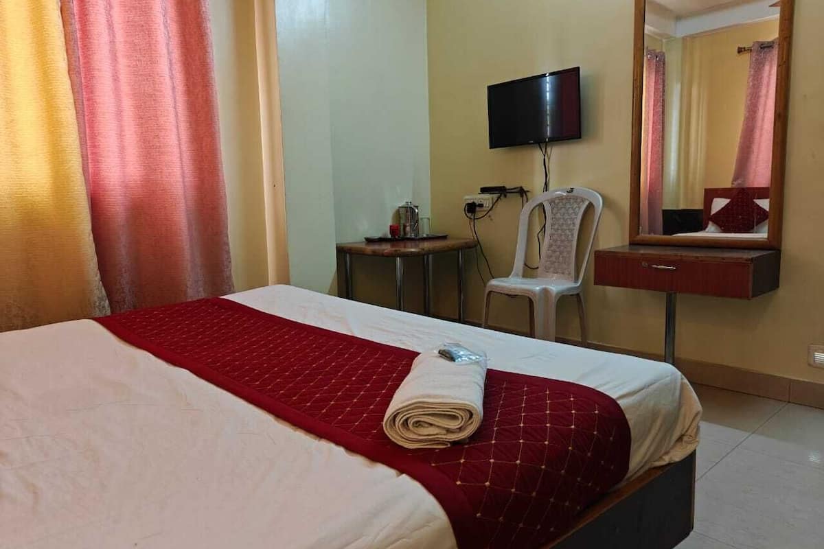 Una camera d'albergo con un letto, una televisione, una poltrona, un tavolino e uno specchio.