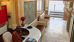 Un espace d’accueil avec un comptoir, un coin salon avec un canapé, un vase de fleurs et un escalier en arrière-plan.