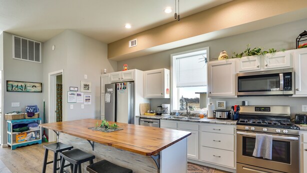 A modern kitchen with white cabinets, a wooden island with stools, stainless steel appliances, and a window with blinds. - Richland Home on Multi-Unit Farm: Fish, Hike! (Richland)