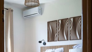 Quarto com cama, ar condicionado, luminária pendente e quadros nas paredes.