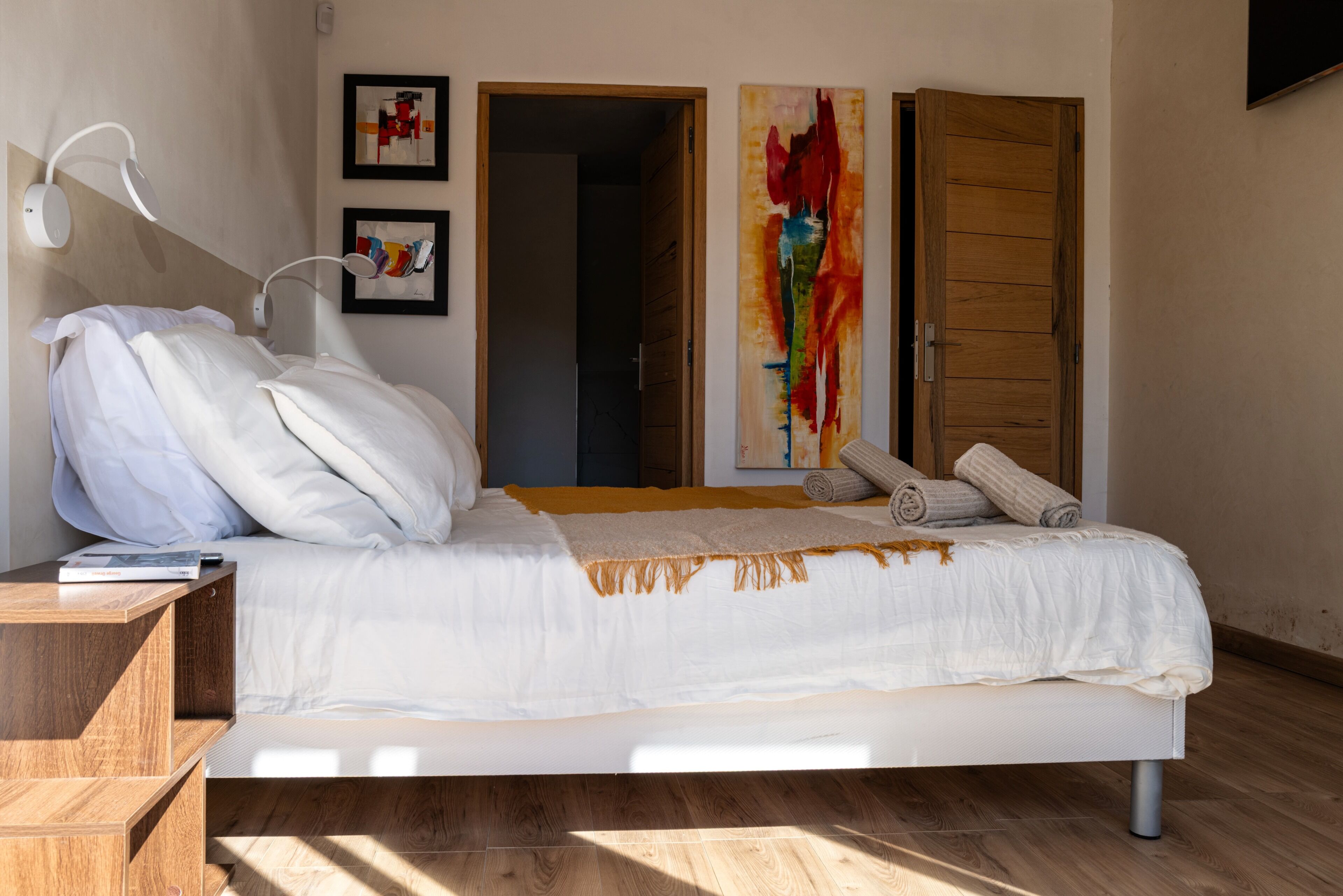A modern bedroom with a bed, bedside tables, a wall-mounted lamp, and artwork.
