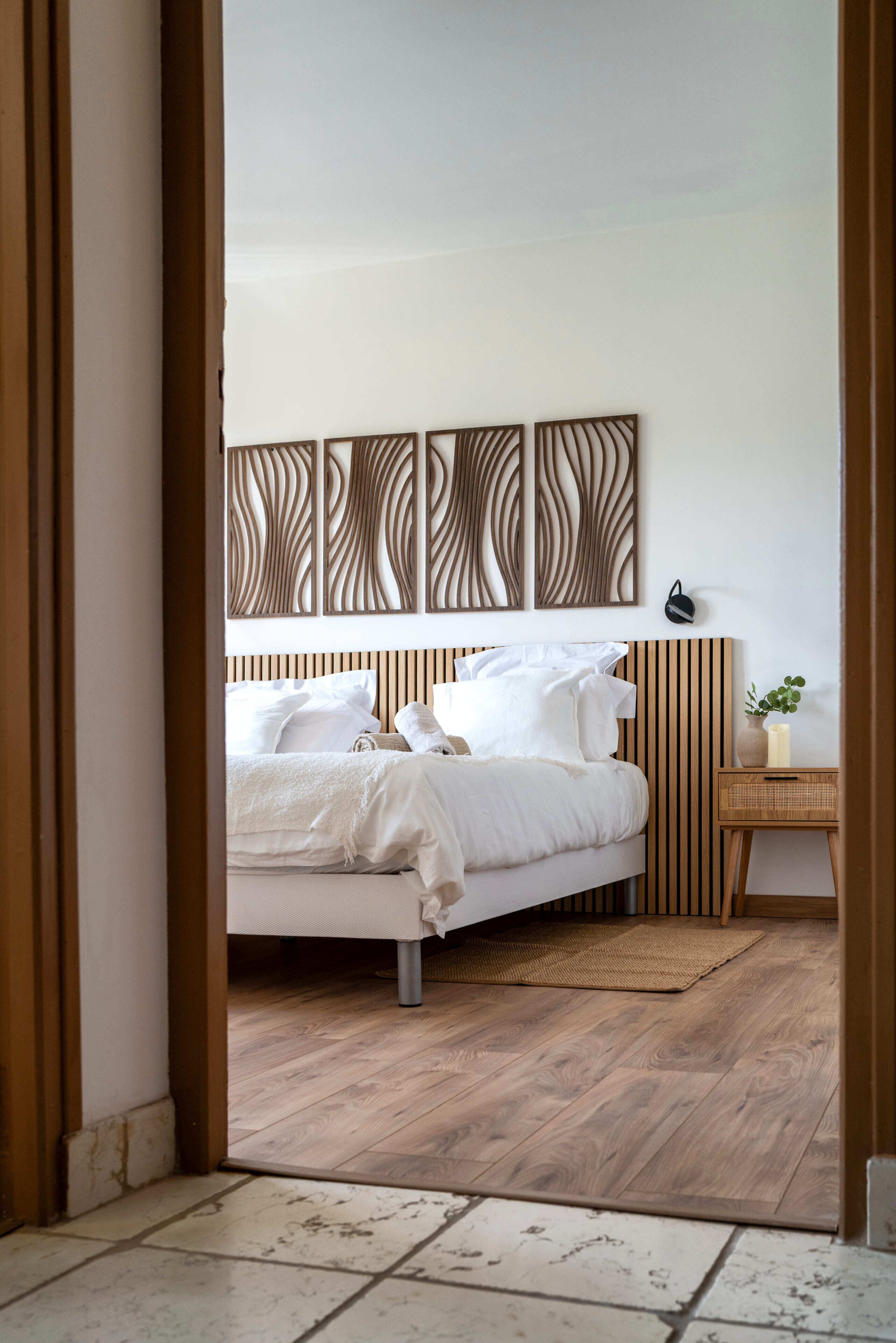 A bedroom with a bed, a bedside table with a plant, and a wall-mounted light fixture.