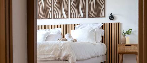 A bedroom with a bed, a bedside table with a plant, and a wall-mounted light fixture.