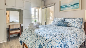 Un dormitorio con cama, una silla, un espejo, un cuadro y una ventana.
